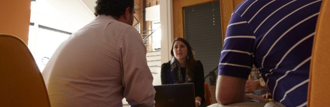 two men and a woman sitting in a living room facing each other talking