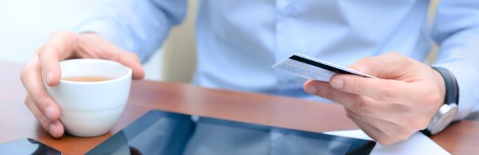 Man with credit card and coffee pondering usage on tablet