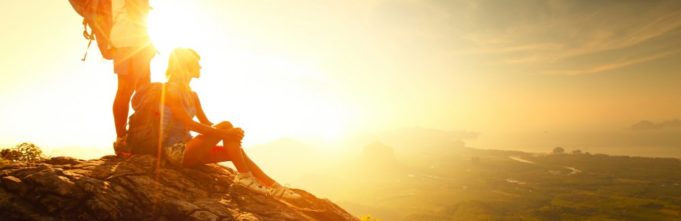 Two people standing on a mountain with a sunset behind them