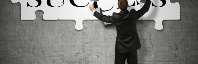 Success written in jigsaw puzzle on wall being put together by man in suit