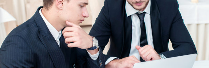 Two men in suits looking at computer and thinking