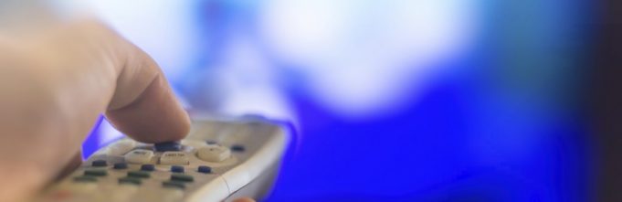 Close up of remote in hand with shallow depth of field during television watching