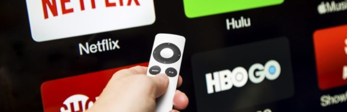 Person holding apple tv controller with netflix, hulu, showtime, and HBO GO on the screen