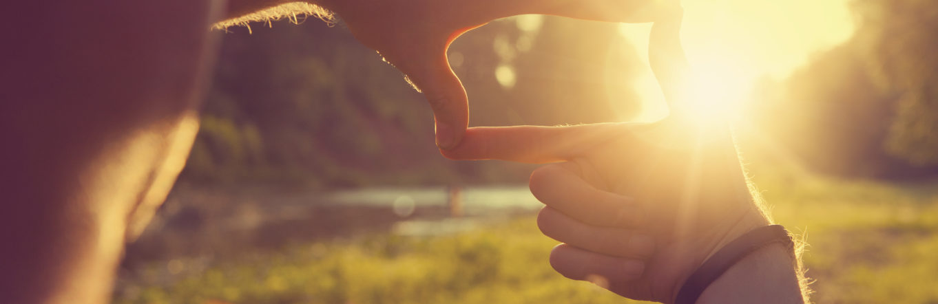 Hands framing distant sun rays
