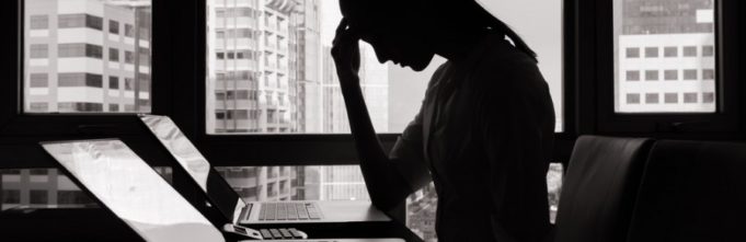 Woman sitting in distress at her desk looking down at her computer