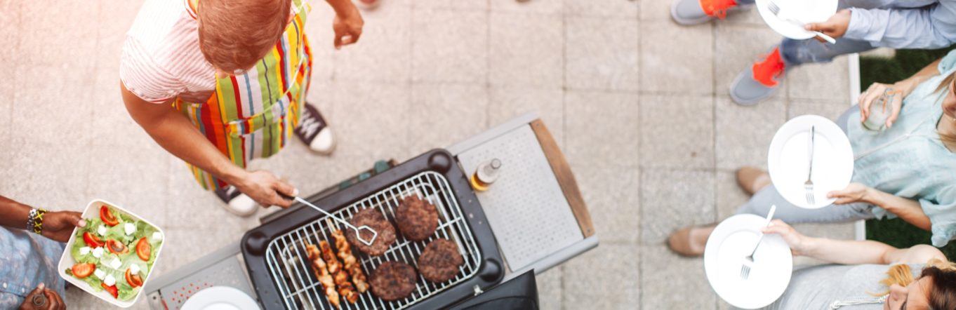 Man grilling outside on a patio with multiple people around him holding plates