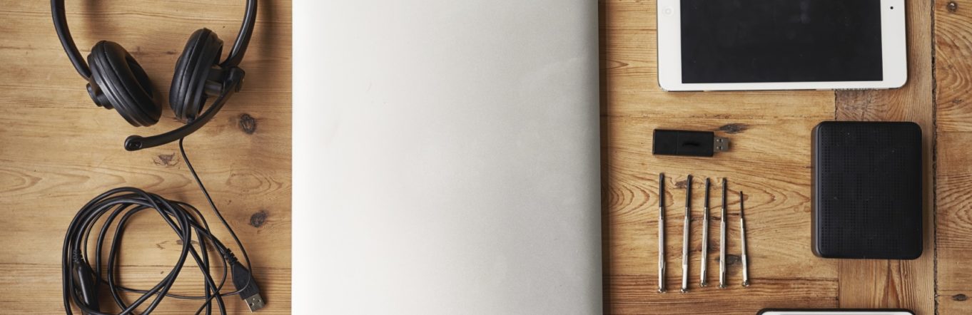 Laptop, ipad, iphone, headphones, and other tech items laid on a wooden table