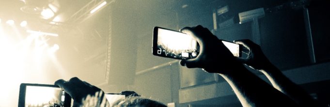 People in a crowd with their phones up recording performers on stage