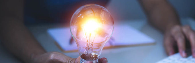 Hand holding a lit lightbulb with a keyboard in the background