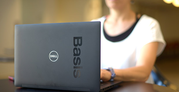 Dell laptop with Basis sticker with female employee sitting behind it, typing.