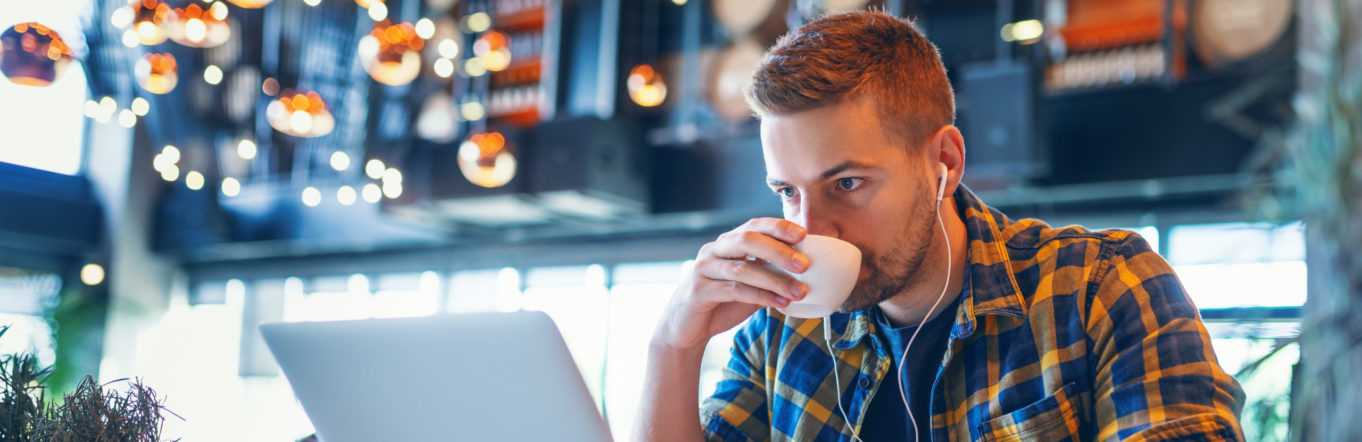 Young man listening to music on laptop online in coffee shop