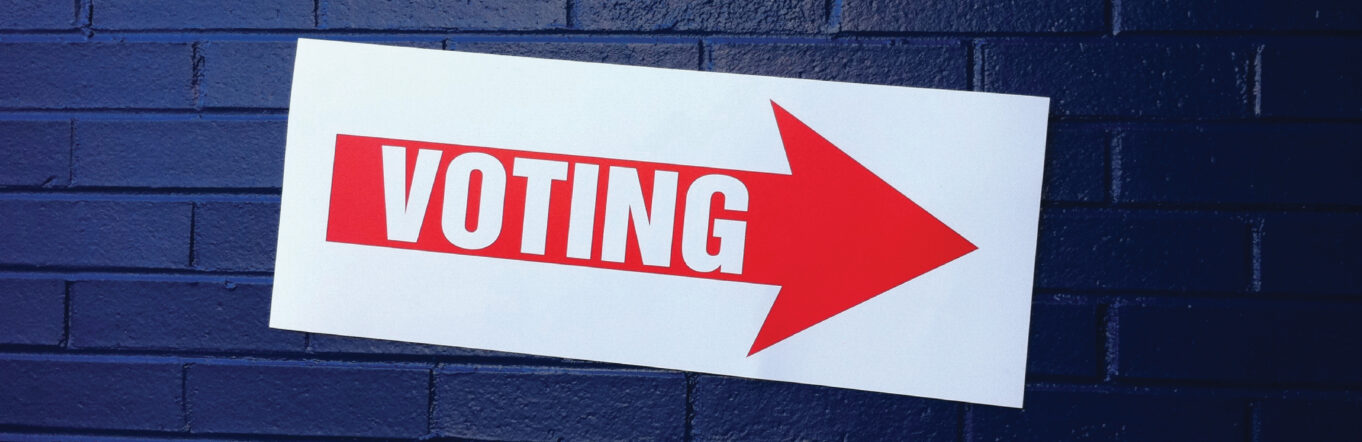 Sign that says "voting" posted on a brick wall