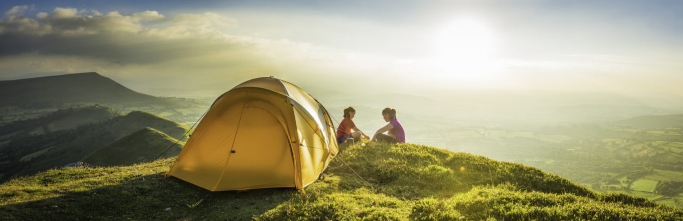 Two women camping at the top of a hill with an orange tent